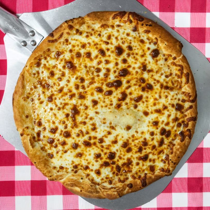 A golden-brown cheese pizza from Sunny's Pizza & Wings on a metal peel over a red and white checkered tablecloth.
