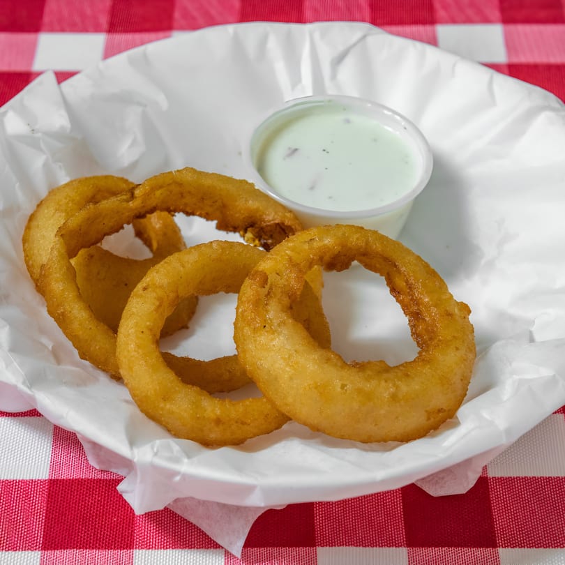 Golden-brown onion rings and a side of creamy dipping sauce in a white paper basket.