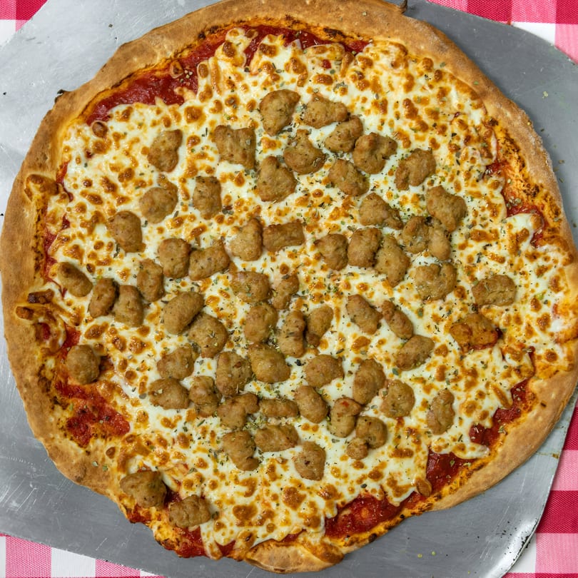 Sunny's Pizza & Wings' sausage pizza, with melted cheese and tomato sauce, on a metal peel.