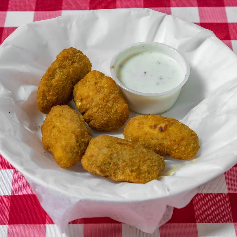 Six golden-brown fried jalapeño poppers and a small cup of ranch dressing in a white basket.